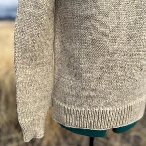 Close-up of a beige knitted sweater on a mannequin against a blurred natural background