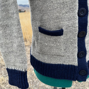 Gray cardigan with navy trim and buttons on a blurred natural background