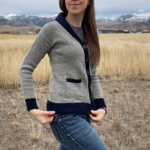 Person wearing a gray cardigan with navy trim in a field with mountains in the background