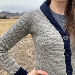 Person wearing a gray and navy cardigan with a mountainous landscape in the background