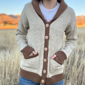 Person wearing a beige and brown cardigan with a blurred natural background