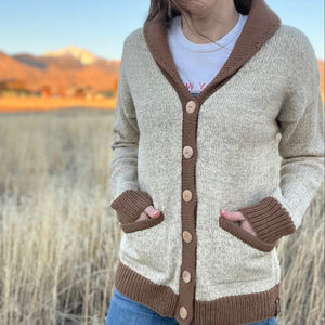 Person wearing a beige and brown cardigan with a scenic background