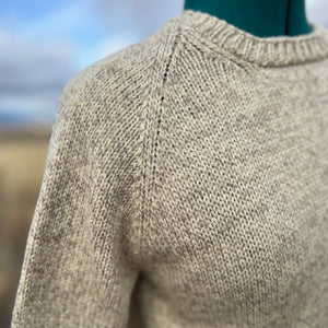 Close-up of a beige knitted sweater with a blurred natural background